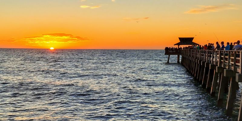 The sun setting over the water beside a long wooden pier