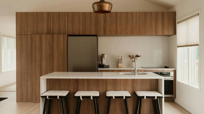 A modern kitchen with a walnut wall of cabinets and a white island with four stools
