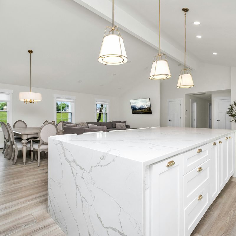 A white kitchen with a marble island and pendant lights